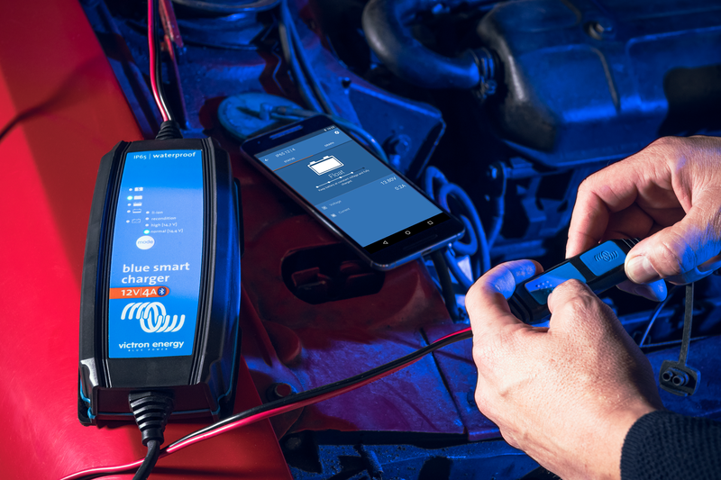Person using a smartphone app to control a blue smart battery charger inside a vehicle.