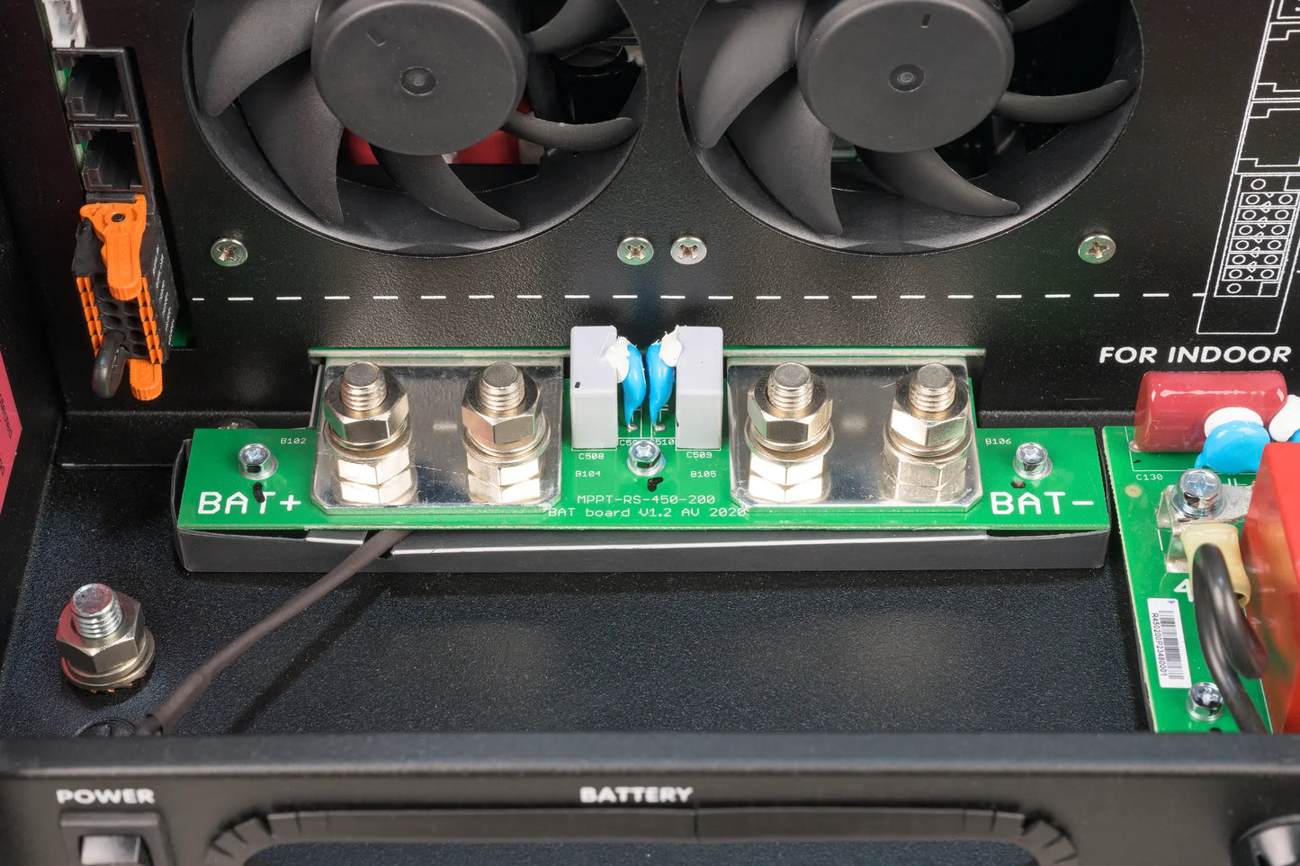 Close-up of a battery connection panel with fans and tools on a black surface.
